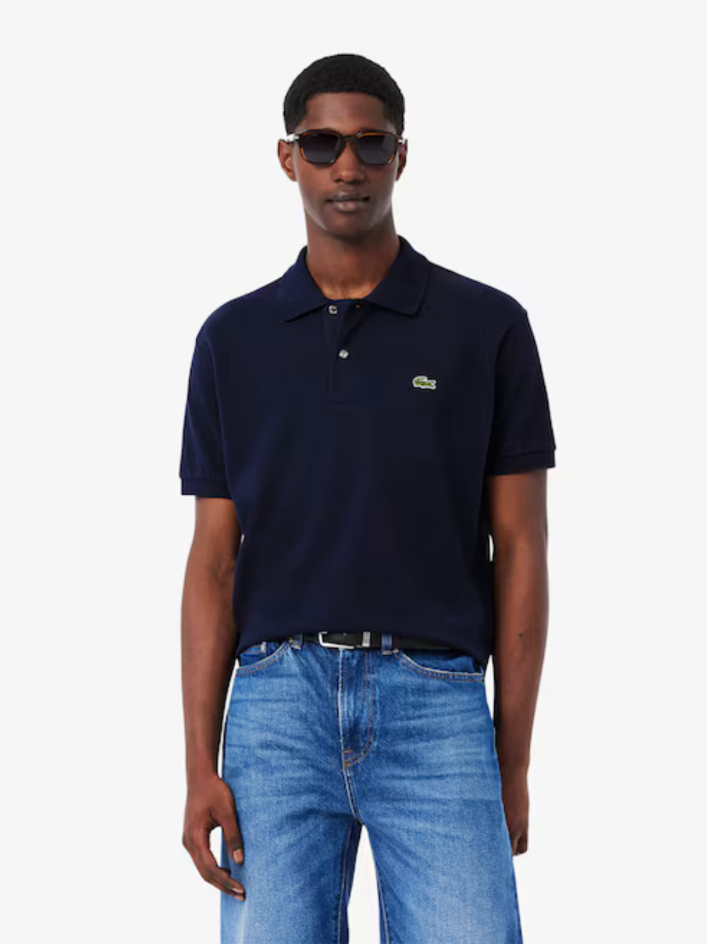 Man wearing a navy polo shirt with a brand logo and blue jeans on a white background