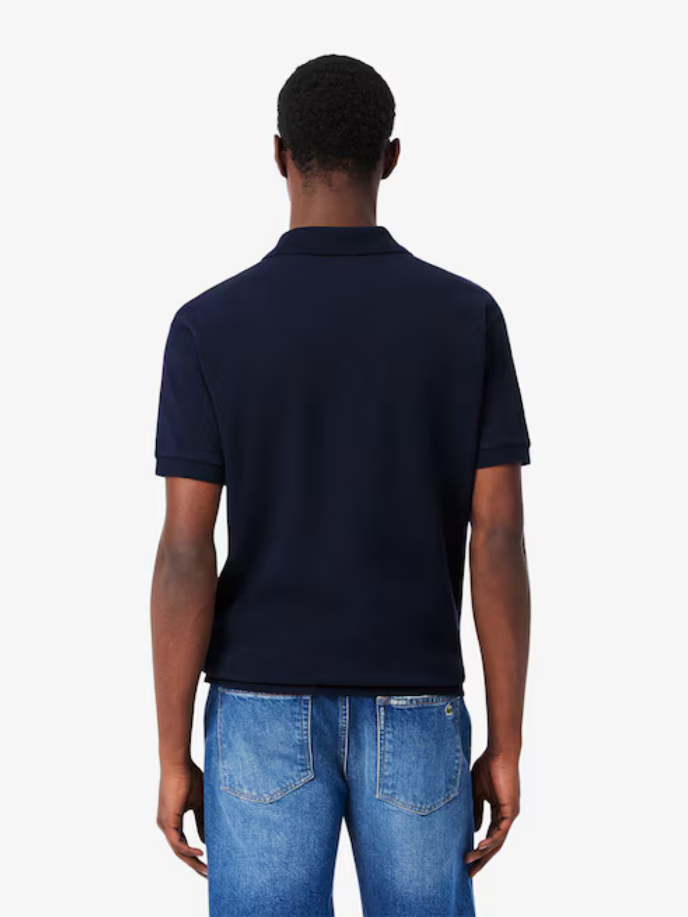 Person wearing a navy blue polo shirt and blue jeans on a white background
